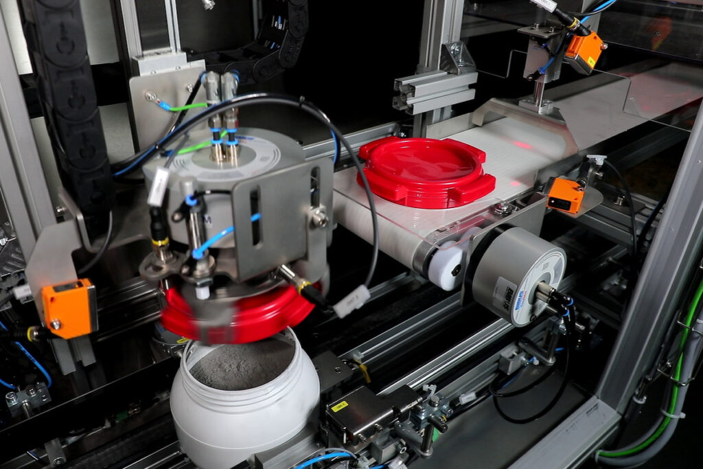 The gripper picks up a lid from the conveyor belt and places it on the container. Then, it screws the lid onto the container with an adjustable amount of torque.