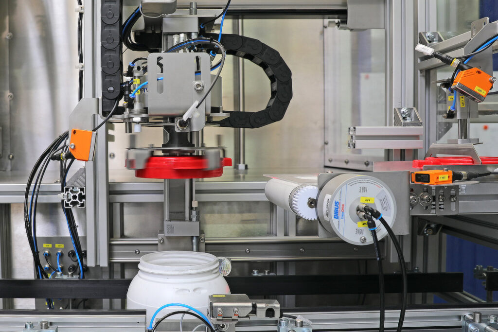 The gripper picks up a lid from the conveyor belt and places it on the container. Then, it screws the lid onto the container with an adjustable amount of torque.